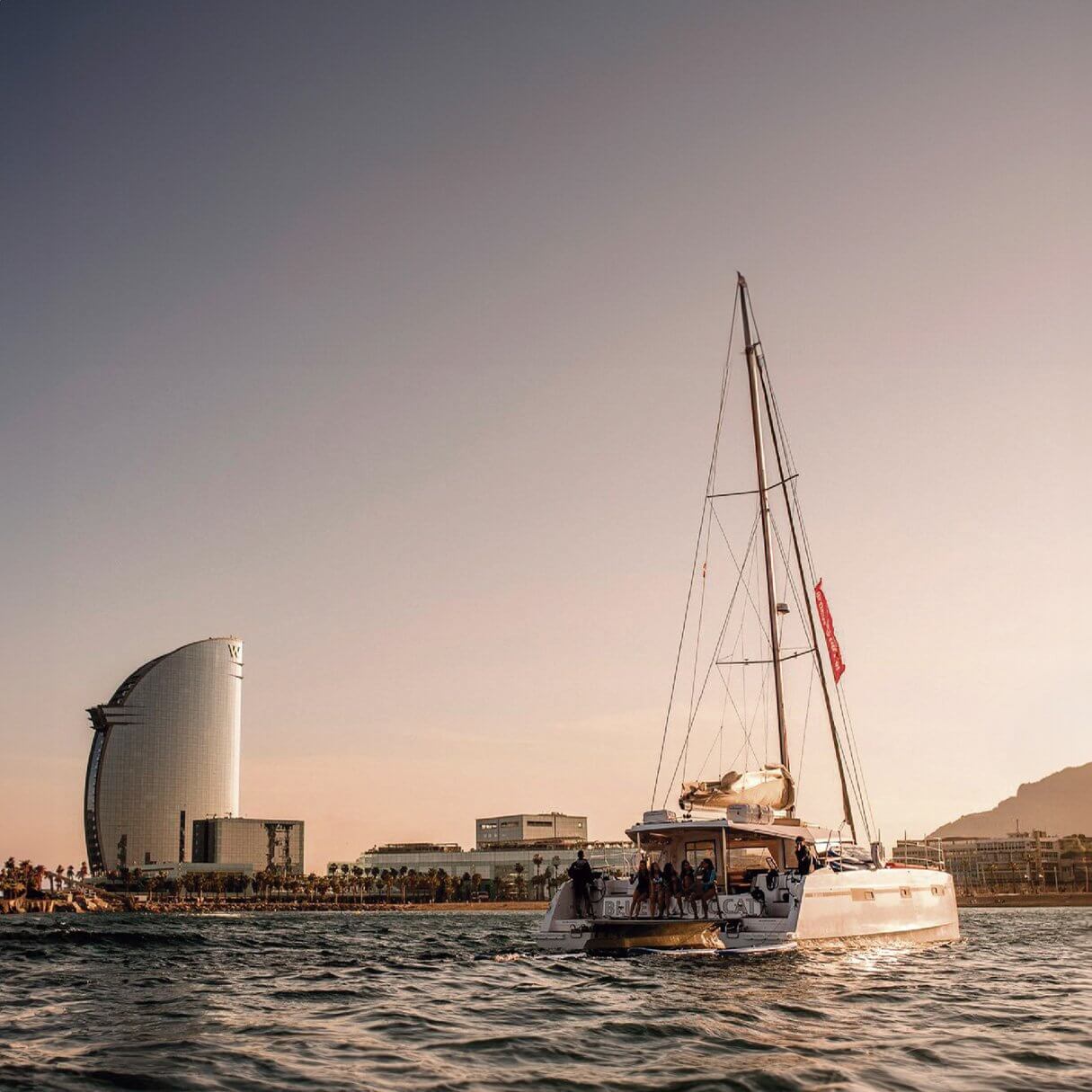 Velero al atardecer con el Hotel W Barcelona de fondo — luz dorada