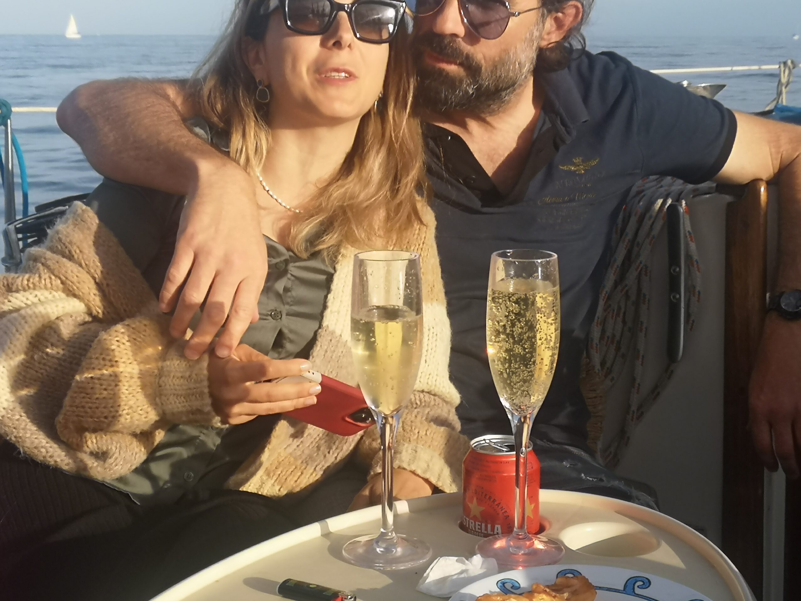 Pareja brindando con cava a bordo del velero frente al skyline de Barcelona